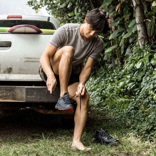 Man sitting on truck bed putting on black athletic shoes with red sole accents.