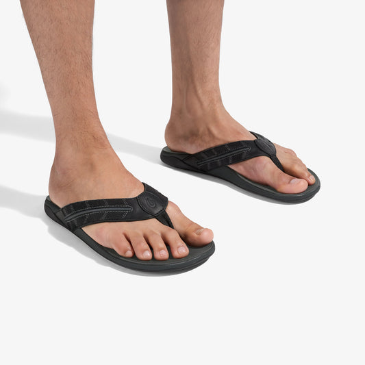 Black thong sandals with textured straps worn on male feet against white background.