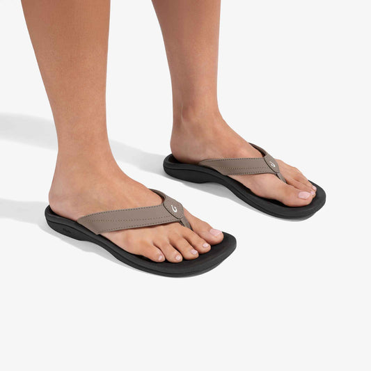 Pair of flip-flop sandals with warm taupe straps and black soles, worn on feet.