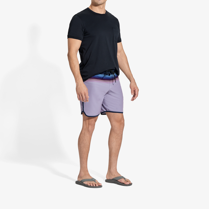 Man wearing black t-shirt, lavender shorts with navy trim, and dark slide sandals.