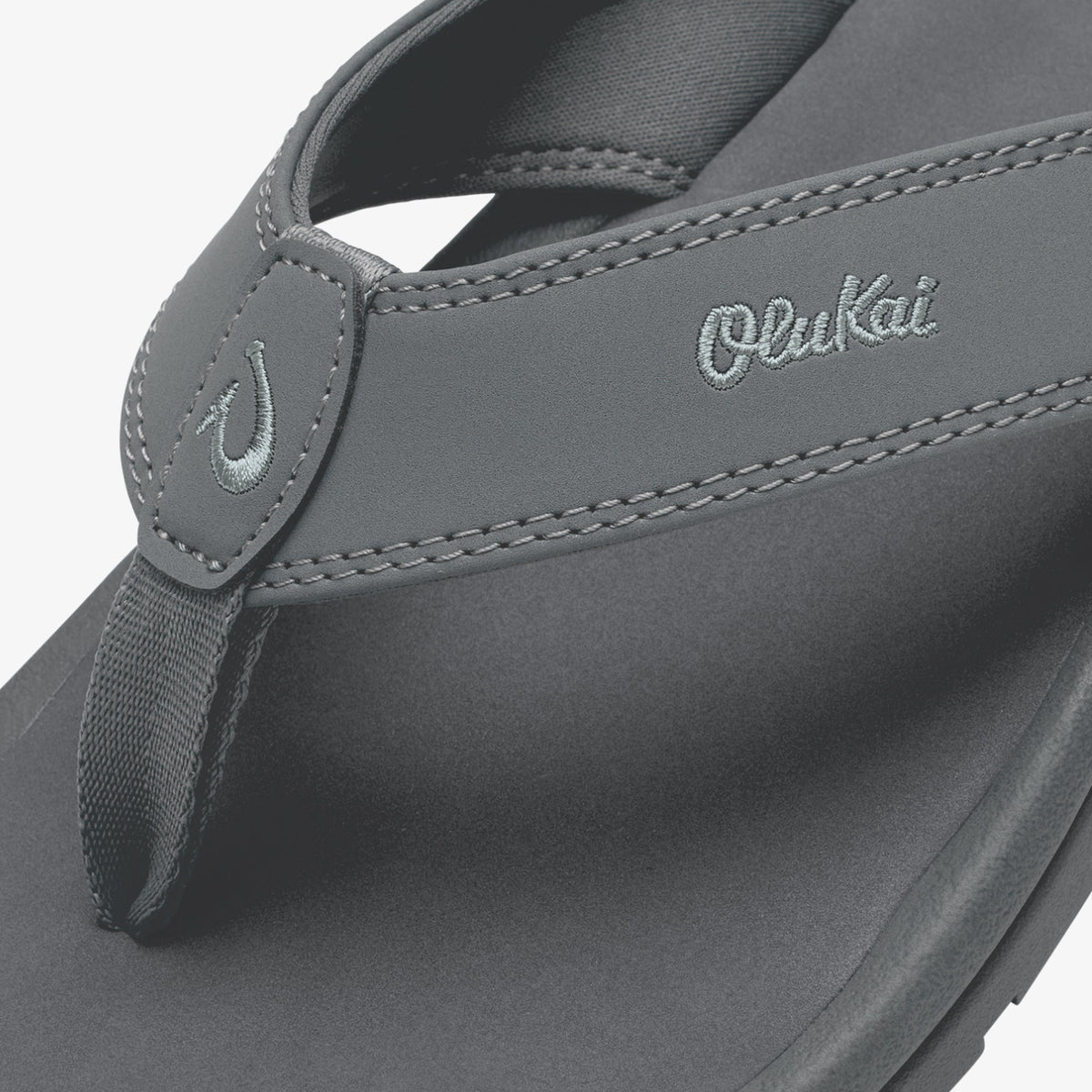 Gray OluKai thong sandal with embroidered logo and contrasting stitching detail on upper strap.