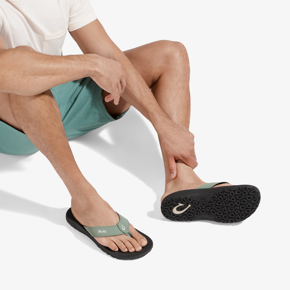 Man wearing seagreen and black sandal with black sole, paired with matching shorts and white shirt.