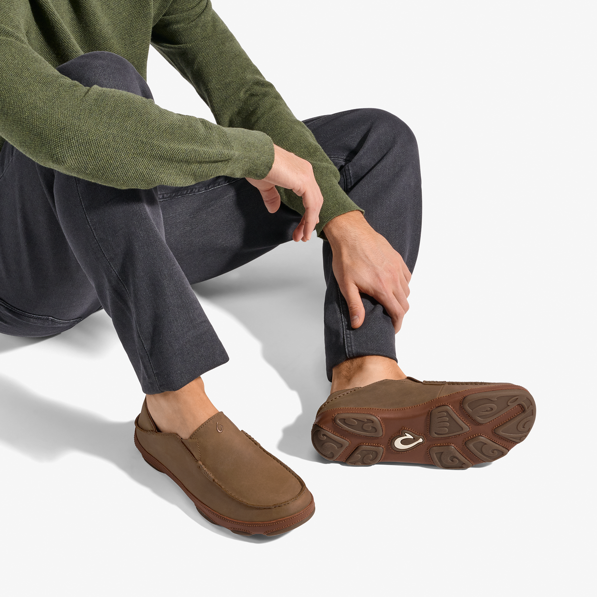 Brown suede slip-on loafer with textured sole, worn with olive sweater and dark jeans.