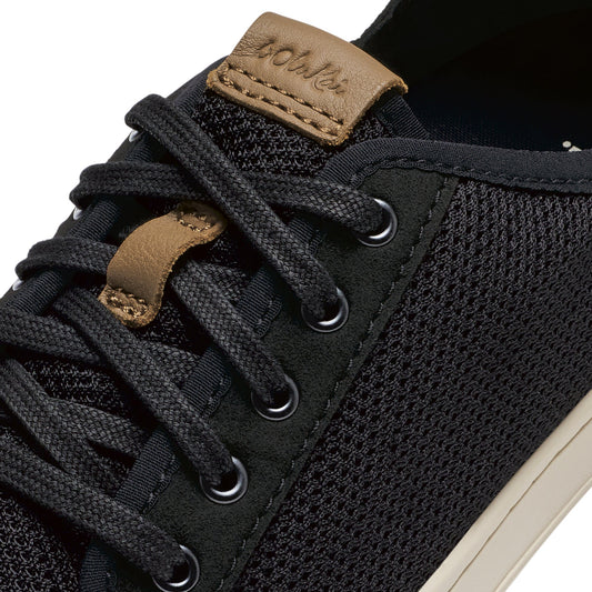 Black knit sneaker with tan leather heel collar and laces, featuring metal eyelets and white sole.