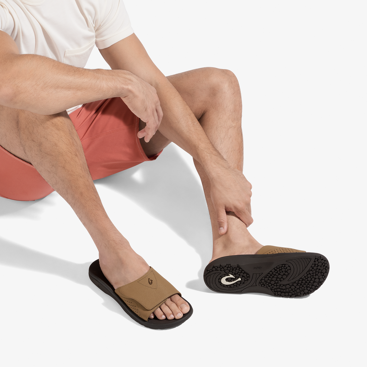 Tan and dark brown slide sandal with black sole worn by man in white shirt and coral shorts.