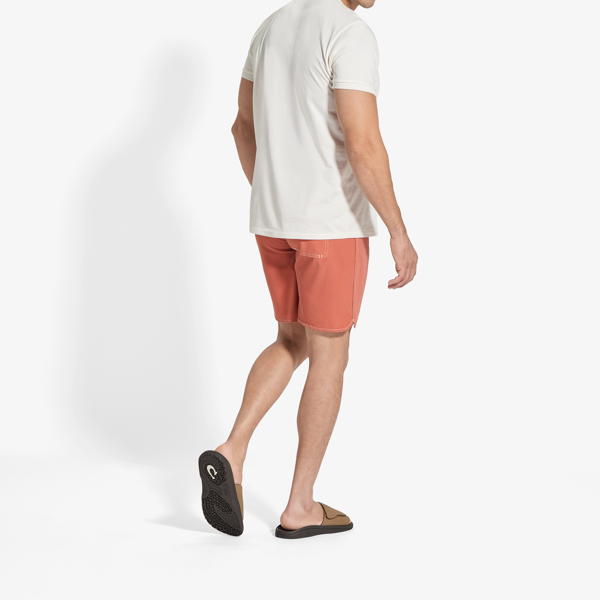 Man wearing tan and dark java Nalu slide sandals with coral shorts and white t-shirt.