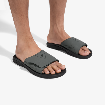 Pair of gray and black slide sandals with perforated details worn on feet.