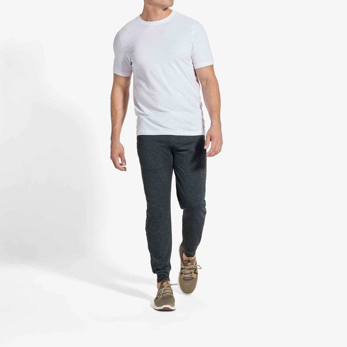 Man wearing white short-sleeve t-shirt, dark gray joggers, and tan lace-up sneakers.