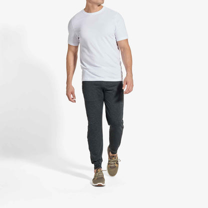 Man wearing white short-sleeve t-shirt, dark gray joggers, and tan lace-up sneakers.