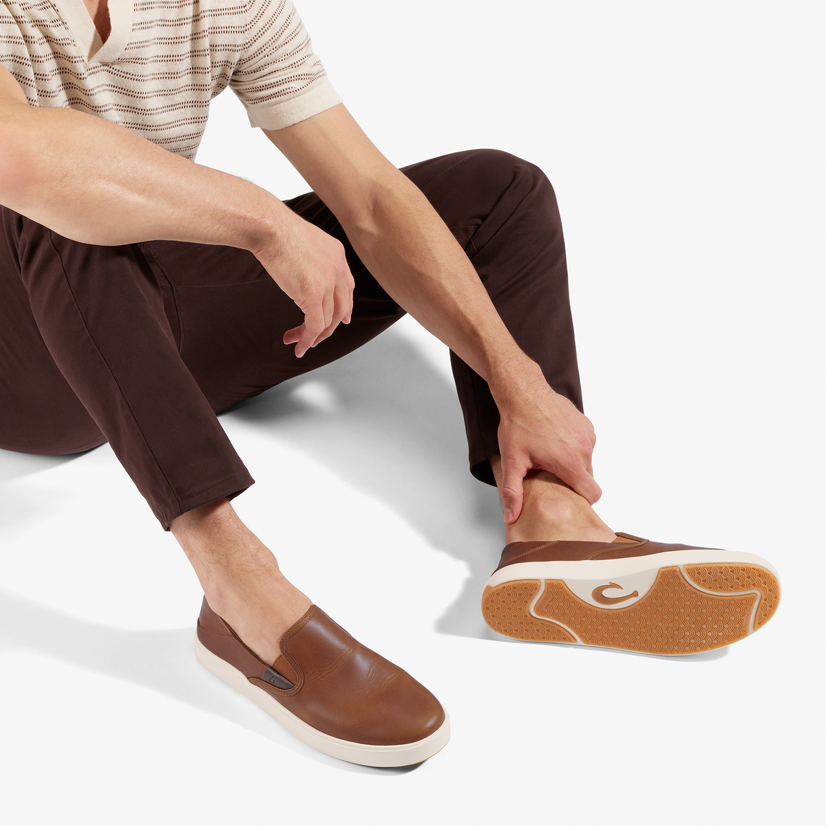 Man wearing striped shirt and brown pants with brown leather slip-on sneaker with white sole.