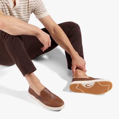 Man wearing striped shirt and brown pants with brown leather slip-on sneaker with white sole.