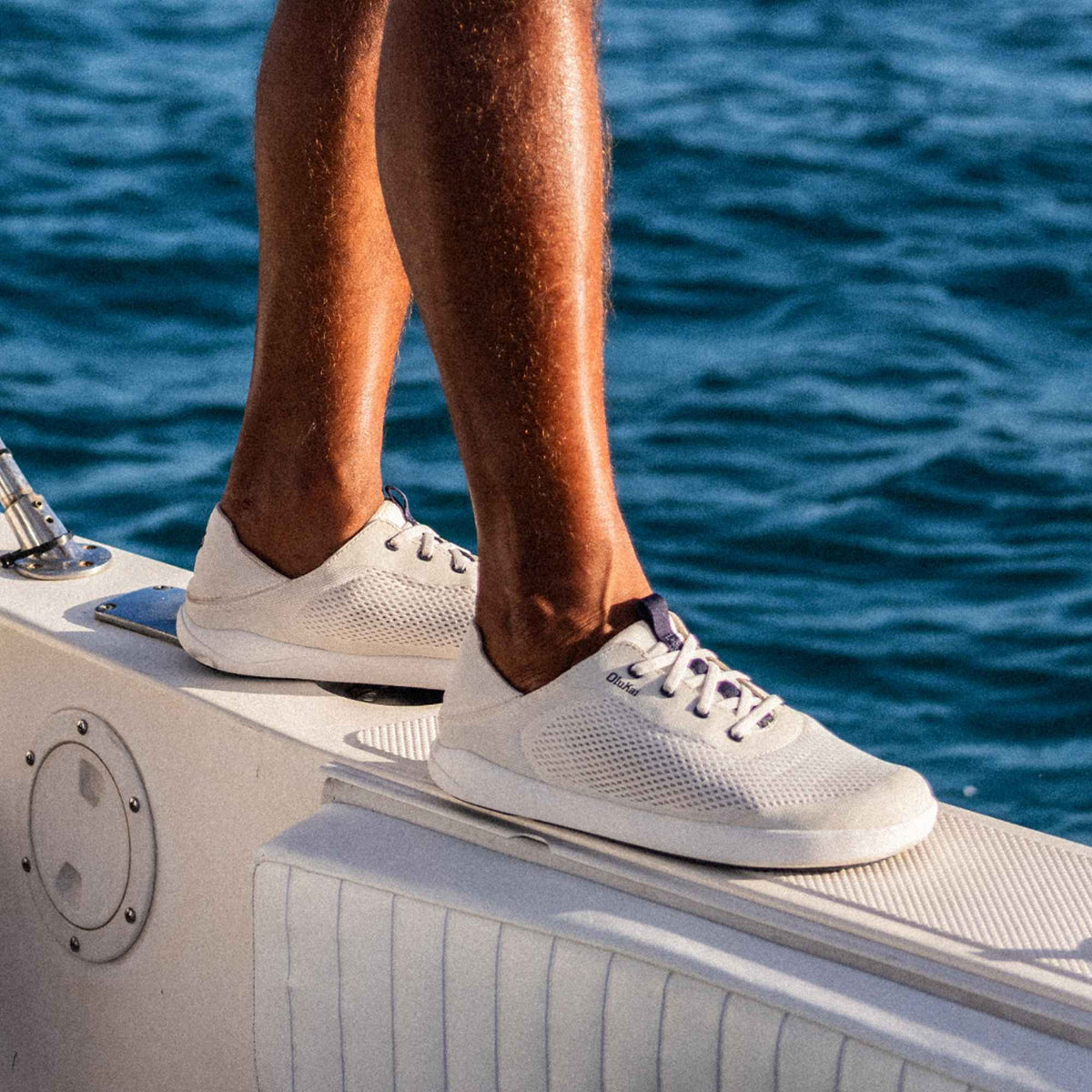 White mesh sneakers with navy laces on a boat deck overlooking ocean water.
