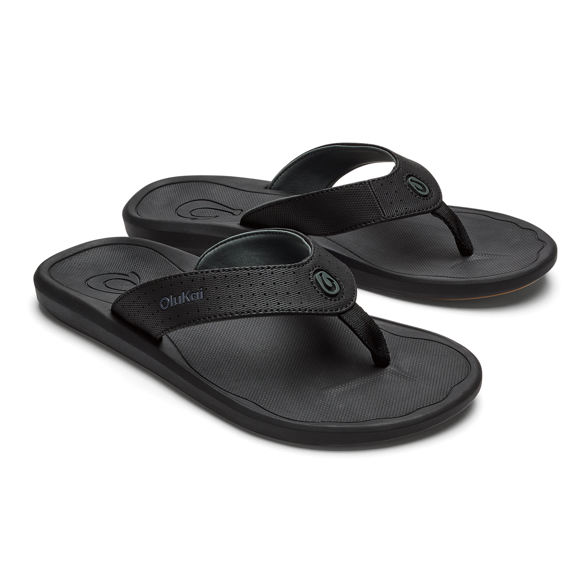 Two black OluKai flip-flops with textured footbeds and woven straps displayed side by side.