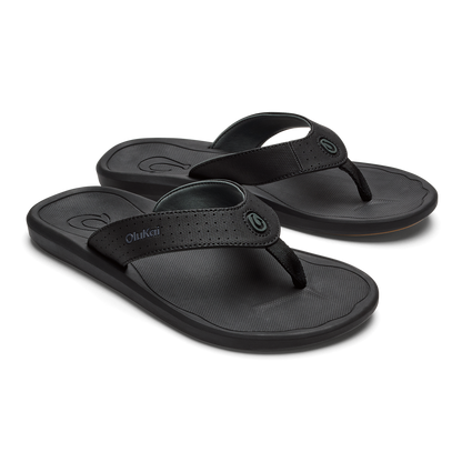 Two black OluKai flip-flops with textured footbeds and woven straps displayed side by side.