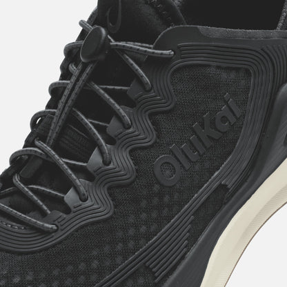 Black athletic shoe with mesh and synthetic upper, dark laces, ridged sole detail, and white midsole accent.