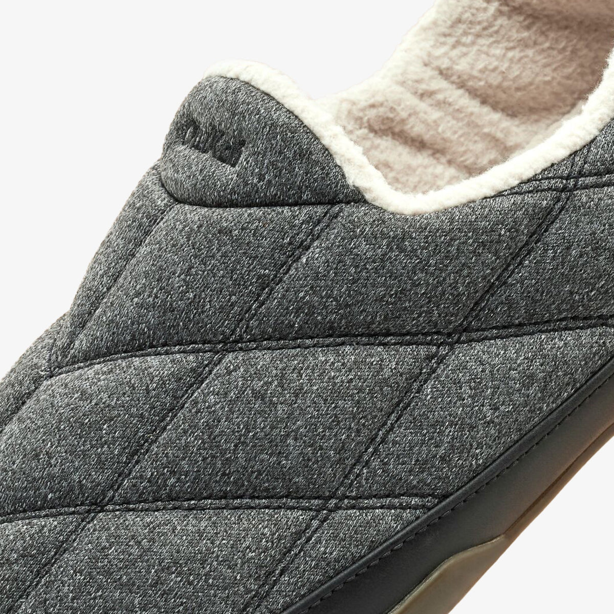 Dark gray quilted slipper with cream fleece lining and dark sole, close-up of heel and upper portion.