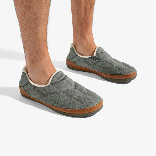Gray quilted slip-on slippers with cream fleece lining and tan rubber sole, worn on bare feet.