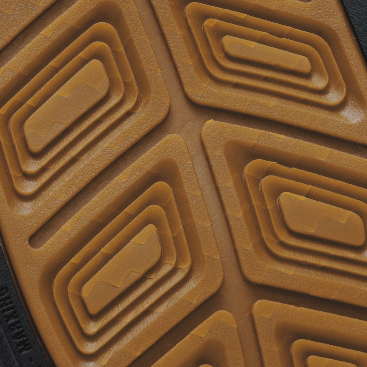 Tan rubber sole with geometric waffle tread pattern and dark material visible at edge.