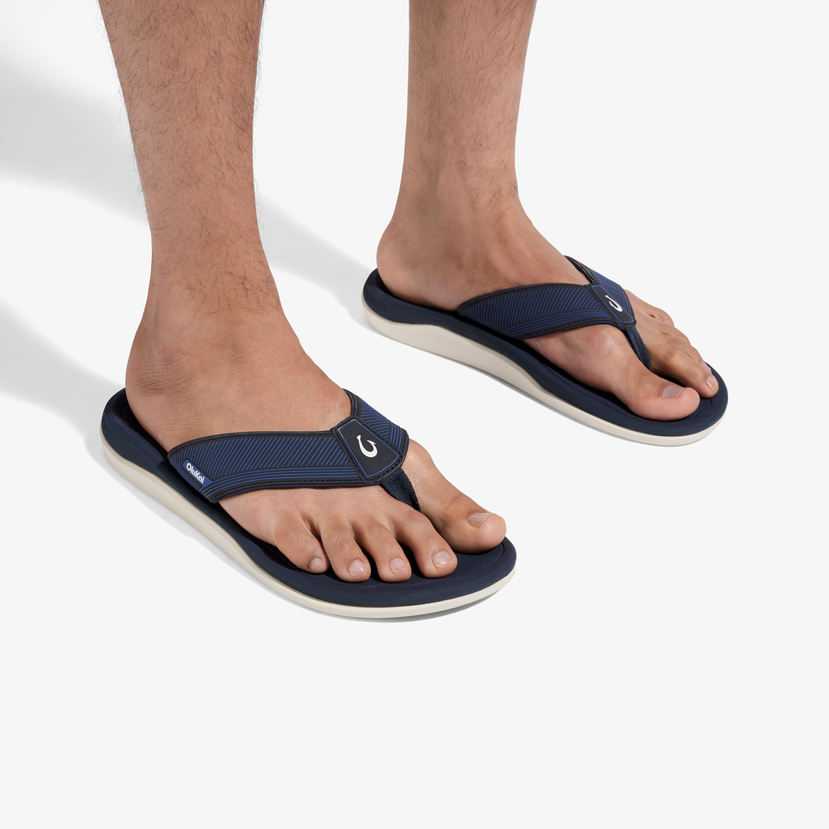 Dark blue thong sandals with cream-colored soles worn on male feet against white background.