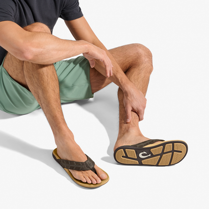 Man wearing dark Java and golden sand sandal with thong strap and cushioned sole, paired with sage green shorts.