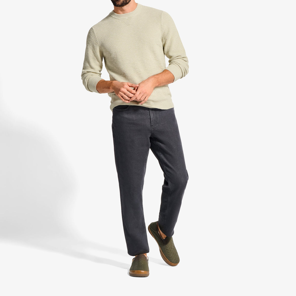 Man wearing a cream crewneck sweater with dark jeans and brown suede shoes.