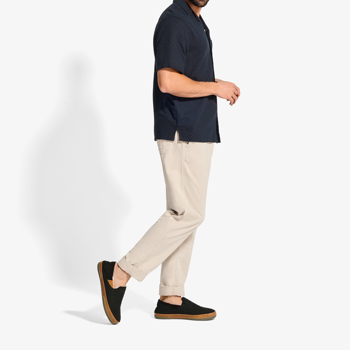 Man wearing black short-sleeve textured shirt with cream pants and black slip-on shoes.