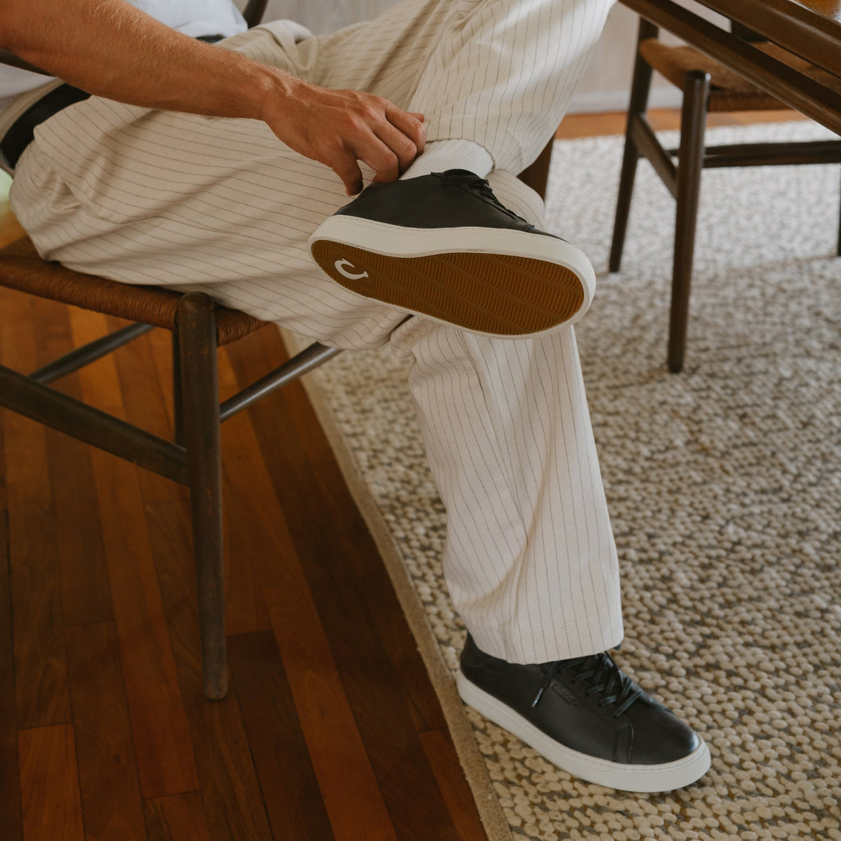 Black and white lace-up sneaker with tan sole, worn with cream pinstriped pants.