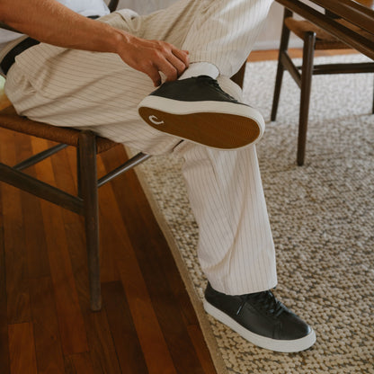 Black and white lace-up sneaker with tan sole, worn with cream pinstriped pants.