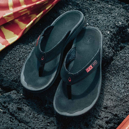 Black thong flip-flops with red accent details and logo patch on textured sole.
