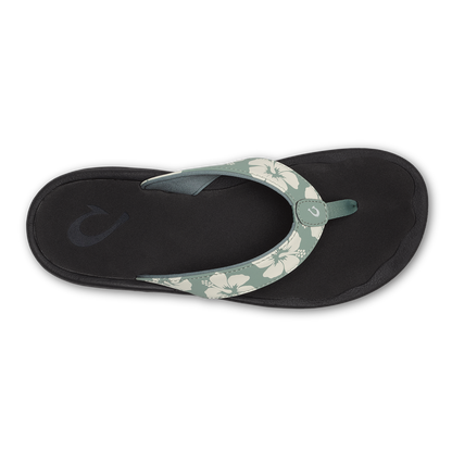 Black flip-flop sandal with sage green floral-patterned strap and circular buckle detail, viewed from above.