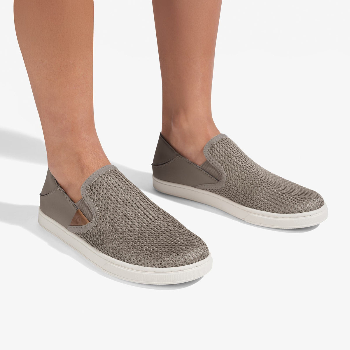 Taupe grey slip-on sneakers with textured knit upper and cream rubber sole, worn on feet.