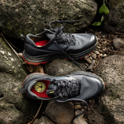 Black and gray trail running shoes with red midsole and accents displayed on lava rock.