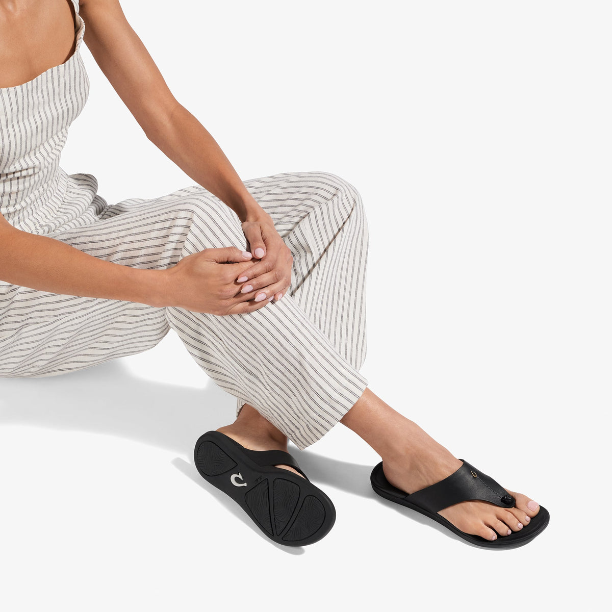 Black slide sandal with curved footbed and thong strap worn with striped pants.