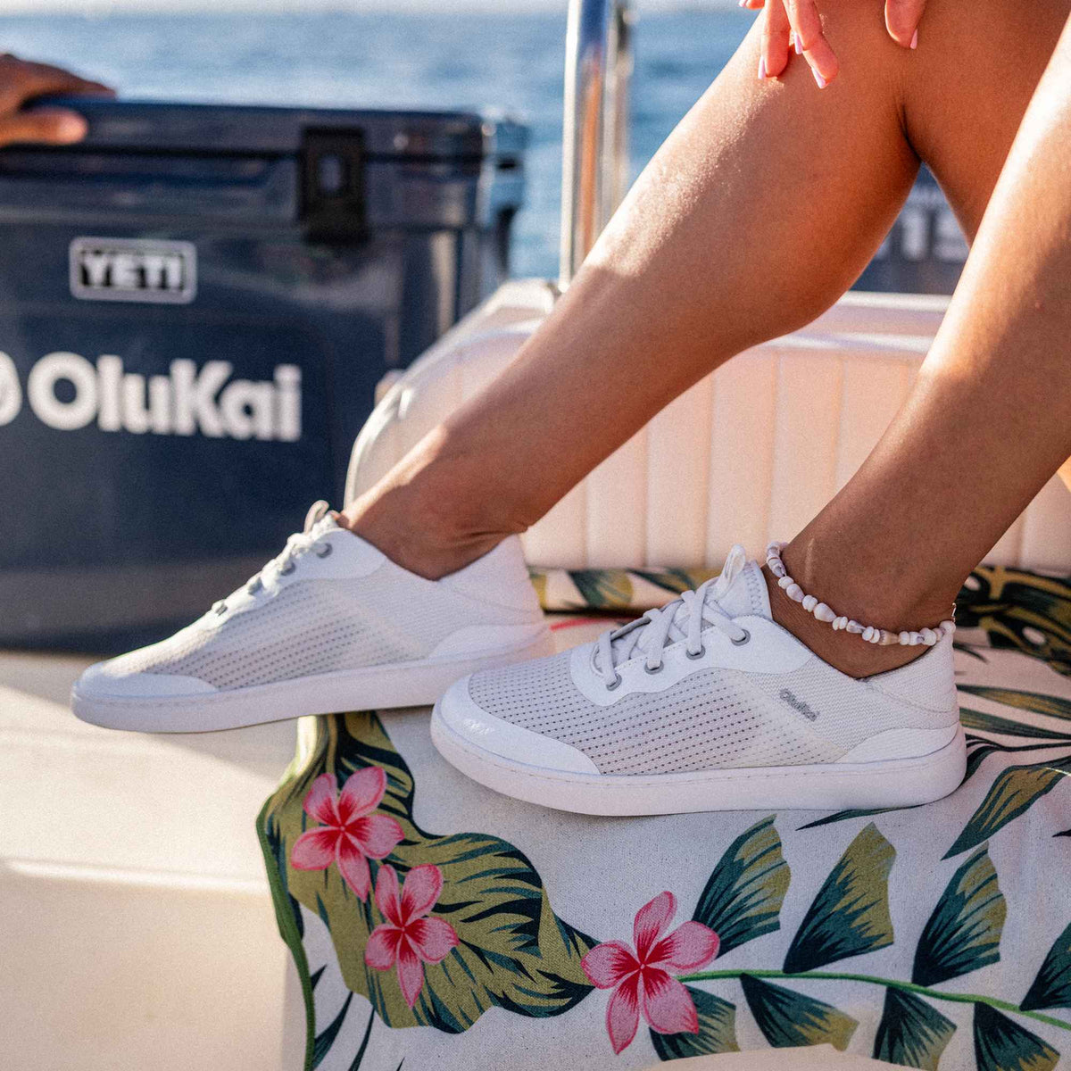 Bright white lace-up sneaker with textured upper and white sole, worn on a boat deck.