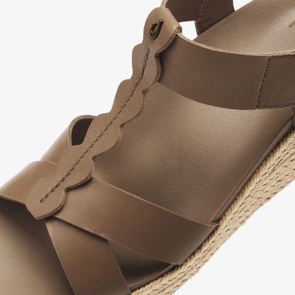 Tan leather sandal with scalloped strap detail and woven jute sole, shown from side angle.
