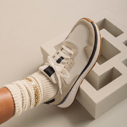 Cream and beige lace-up sneaker with mesh and leather upper, white sole, and black stripe detail on foot.