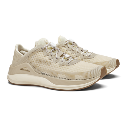 Cream and tan running shoe with textured upper, rhinestone lace detailing, and curved sole design.