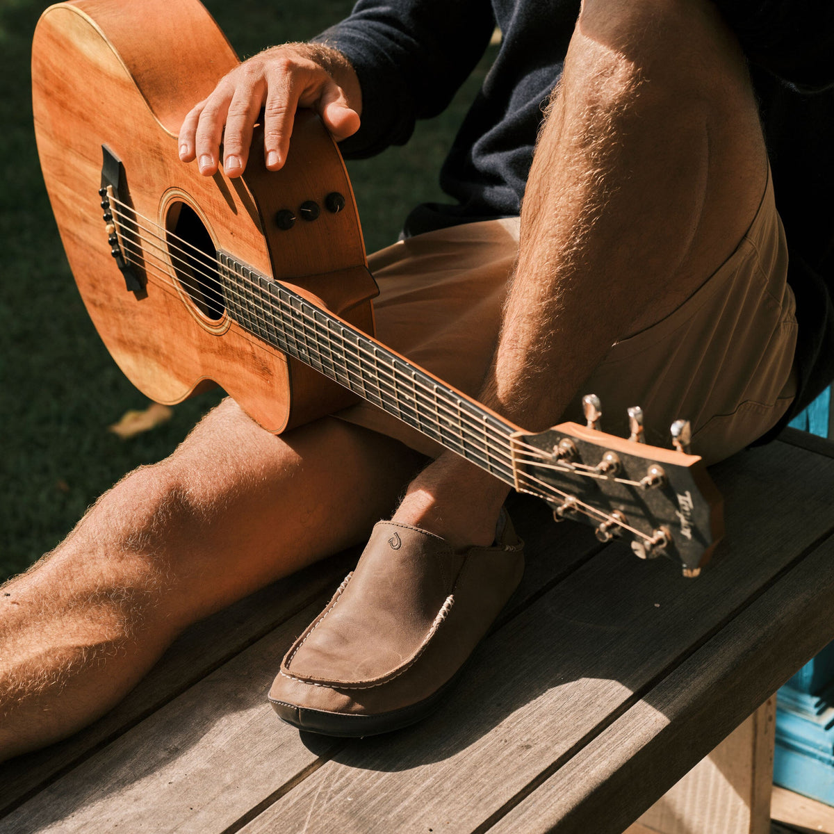 Toffee-colored suede slipper with dark sole worn by person holding acoustic guitar.