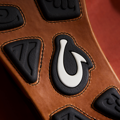 Tan leather with black embossed numerals and white horseshoe detail, orange topstitching visible.