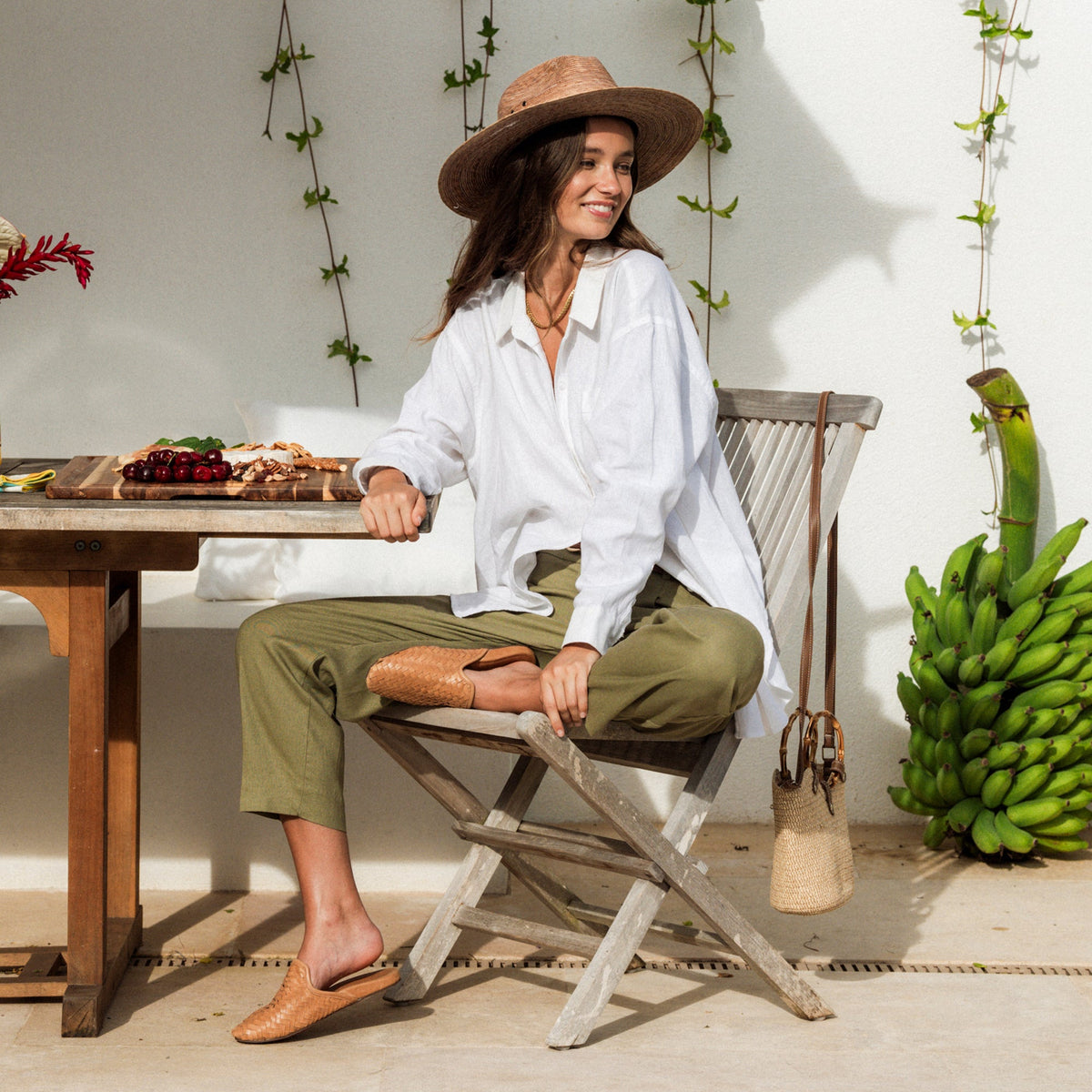 Woman wearing brown woven hat and tan woven slip-on sandals, seated outdoors.